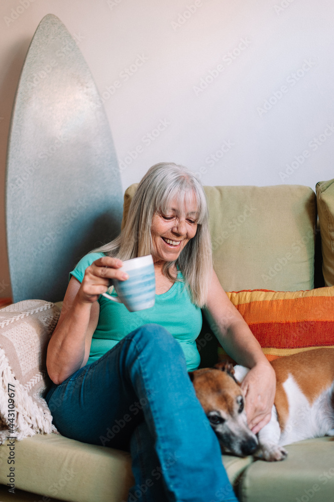 Elder woman having a cup of coffee with her dog while sitting on sofa ...