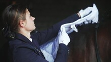 Blond Girl Placing A Saddle Pad On Her Horseback. Back View Of A Girl Wearing A Black Coat And Gloves. Preparing For The Competition Concept. Protecting Horseback. 