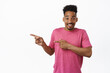 © Cookie Studio - Check out. Happy african american man pointing fingers left at sale logo, showing promo text and smiling cheerful, recommending product, white background