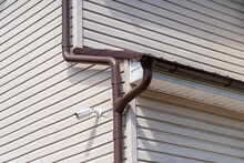 Circuit TV CCTV Security Camera Mounted On Corner Of Building With Siding Facade Next To Brown Gutter Pipe