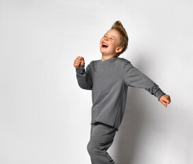 Little boy child with european appearance studio shot in motion. Preteen blond male child wearing trendy sportswear fooling around running away loudly laughing. Happiness and carefree emotion