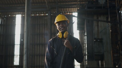 Wall Mural - Portrait American industrial black young worker man smiling with helmet and ear protection in front machine, Engineer standing holding wrench on his shoulder at work in industry factory.