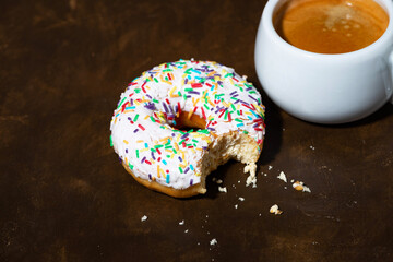 Wall Mural - sweet donut with white frosting and cup of fresh coffee on dark background, top view