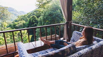 A young woman lying and relaxing on sofa while looking at a beautiful nature view