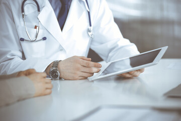 Unknown male doctor and patient woman discussing something while sitting in clinic and using tablet computer. Best medical service in hospital, medicine, pandemic stop