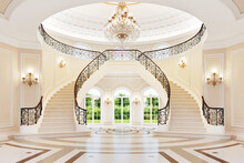 Luxurious Royal Interior With A Beautiful Staircase And Chandelier. Bright Large Hall With Large Windows