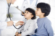 © Iryna - Woman-doctor examining a child patient by stethoscope. Cute arab toddler and his brother at physician appointment. Medicine concept