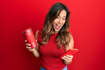 Poster - Young latin woman using smartphone and drinking a cup of coffee celebrating crazy and amazed for success with open eyes screaming excited.