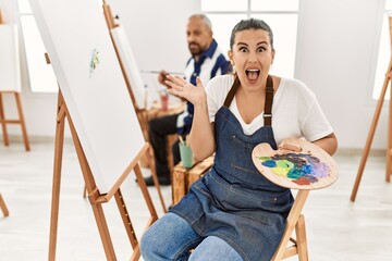 Poster - Young artist woman at art studio celebrating victory with happy smile and winner expression with raised hands