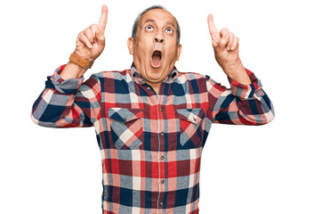 Poster - Senior hispanic man wearing casual clothes amazed and surprised looking up and pointing with fingers and raised arms.