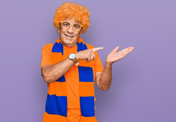 Wall Mural - Senior hispanic man football hooligan cheering game amazed and smiling to the camera while presenting with hand and pointing with finger.