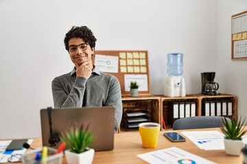 Poster - young hispanic man wearing business style sitting on desk at office looking confident at the camera 