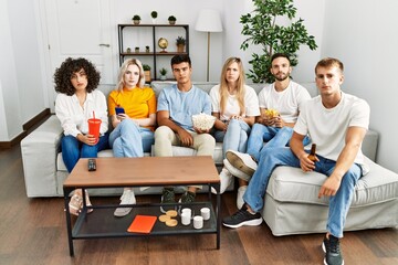 Wall Mural - Group of people eating snack sitting on the sofa at home thinking attitude and sober expression looking self confident