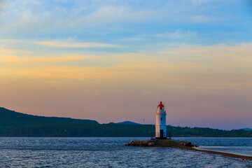 Wall Mural - Tokarevsky lighthouse in Vladivostok. Old white lighthouse on the background of the sea and the green island. Marine landmark of the Primorsky region.