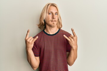 caucasian young man with long hair doing rock gesture relaxed with serious expression on face. simpl