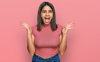 Poster - Young hispanic girl wearing casual t shirt celebrating crazy and amazed for success with arms raised and open eyes screaming excited. winner concept