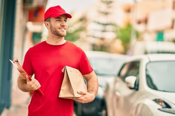 Sticker - Young caucasian deliveryman smiling happy holding delivery paper bag at the city.