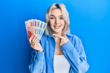 Sticker - Young blonde girl holding new taiwan dollars banknotes smiling happy pointing with hand and finger