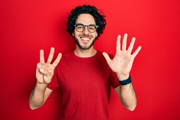 Canvas Print - Handsome hispanic man wearing casual t shirt and glasses showing and pointing up with fingers number eight while smiling confident and happy.