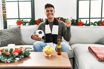 Sticker - Young hispanic man football hooligan holding ball and beer smiling happy pointing with hand and finger to the side