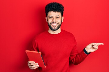 Sticker - Young arab man with beard using touchpad device smiling happy pointing with hand and finger to the side