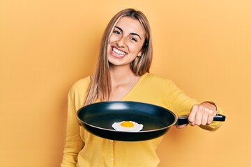 Poster - Beautiful hispanic woman cooking fried egg looking positive and happy standing and smiling with a confident smile showing teeth