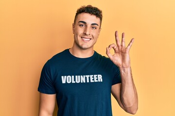 Hispanic young man wearing volunteer t shirt smiling positive doing ok sign with hand and fingers. successful expression.