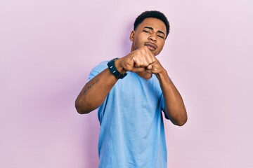 Young african american man wearing casual blue t shirt punching fist to fight, aggressive and angry attack, threat and violence