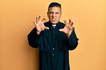 Canvas Print - Young latin priest man standing over yellow background smiling funny doing claw gesture as cat, aggressive and sexy expression