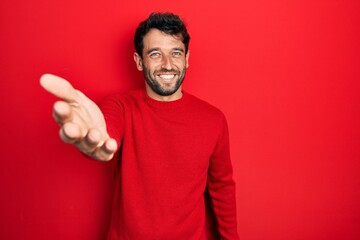 Sticker - Handsome man with beard wearing casual red sweater smiling cheerful offering palm hand giving assistance and acceptance.