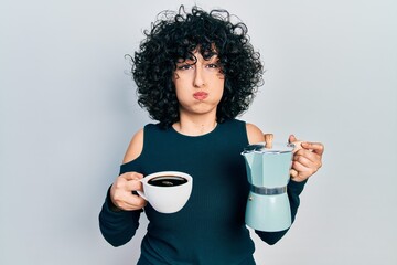 Canvas Print - Young middle east woman holding italian coffee maker puffing cheeks with funny face. mouth inflated with air, catching air.