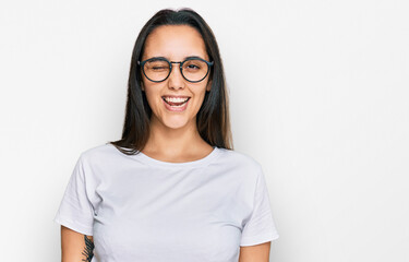 Young hispanic woman wearing casual white t shirt winking looking at the camera with sexy expression, cheerful and happy face.