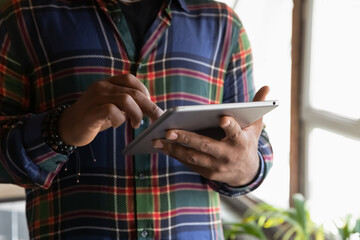 Close up cropped of African American man using tablet modern device apps, typing on screen, young male writing message in social network, chatting or working online, holding gadget in hands