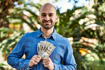 Poster - Young hispanic man smiling happy holding dollars at the park