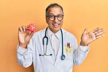 Canvas Print - Middle age indian man wearing doctor coat holding virus toy celebrating victory with happy smile and winner expression with raised hands