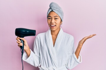 Sticker - Young chinese woman wearing shower towel cap and bathrobe holding dryer celebrating victory with happy smile and winner expression with raised hands