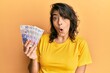 © Krakenimages.com - Young hispanic woman holding 20 polish zloty banknotes scared and amazed with open mouth for surprise, disbelief face