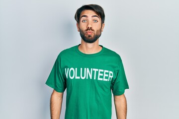 Young hispanic man wearing volunteer t shirt looking at the camera blowing a kiss on air being lovely and sexy. love expression.