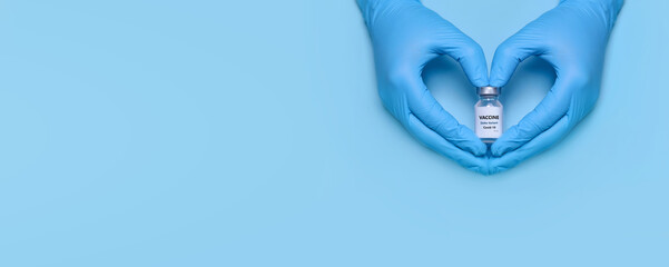 Doctor's hands in protective medical gloves hold a bottle of coronavirus vaccine in a heart-shaped gesture on a blue background. Vaccination. Immunization. Fighting the pandemic. Banner. Copy space