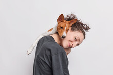 Female Pet Owner Plays With Favorite Dog Which Leans On Her Head Being Best Friends Spend Time Together Dressed In Casual T Shirt Isolated Over White Background. Animals People Friendship Concept