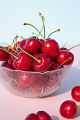 Wall Mural - Close-up of fresh, juicy, organic cherries in a glass bowl against a pink pastel background. Seasonal, summer berries and fruits. Harvesting. Vertical photo