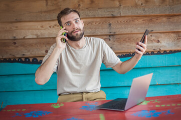 Young crazy hipster talking on the mobile smart phone, using tablet and looking on laptop. Internet connection, networking. Device electronics gadget concept