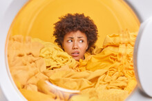 Puzzled Displeased Curly Afro American Woman Housekeeper Looks Away Drowned In Yellow Dirty Laundry Gets Out Cleaned Clothes From Washing Machine Fed Up Of Daily Routine And Domestic Chores.
