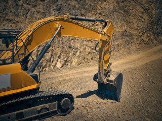 View of excavator jib and scoop opposite foundation pit. Earthmoving machinery at construction site