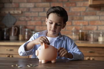 Focused school kid saving money for purchase, putting cash in pink piggy bank at home. Preschooler child learning to calculate personal budget, manage finance, playing investment, accounting