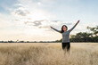 © Lumine Captis - Young adult Mexican smiling woman standing with open arms in a dry grassy meadow