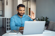 Indian Arabian mature business man wearing wireless earphones waving hand giving greeting gesture looking to personal teacher. Online webinar, videoconference entrepreneur call with student at laptop