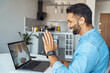 Mature eastern Indian man sitting at home desk front of laptop greeting business partner on screen. 40s freelance entrepreneur businessman communicate remotely online with colleague using pc computer