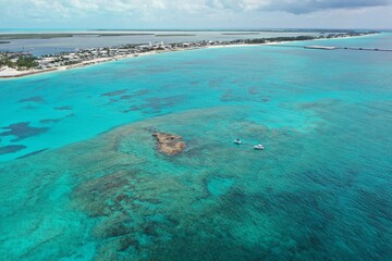 Aerial view of boats anchored near coral rocks with North Bimini coast in background on sunny summer afternoon.