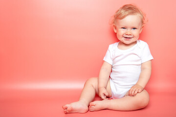 portrait caucasian curly blond smiling baby girl sitting on pink background wearing in white t-shirt